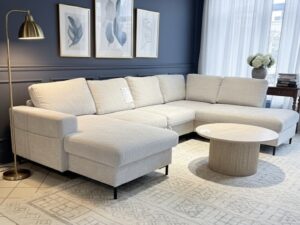 Canapé d'angle beige dans un salon bleu marine élégant avec tapis à motifs, table bois et lampe dorée.