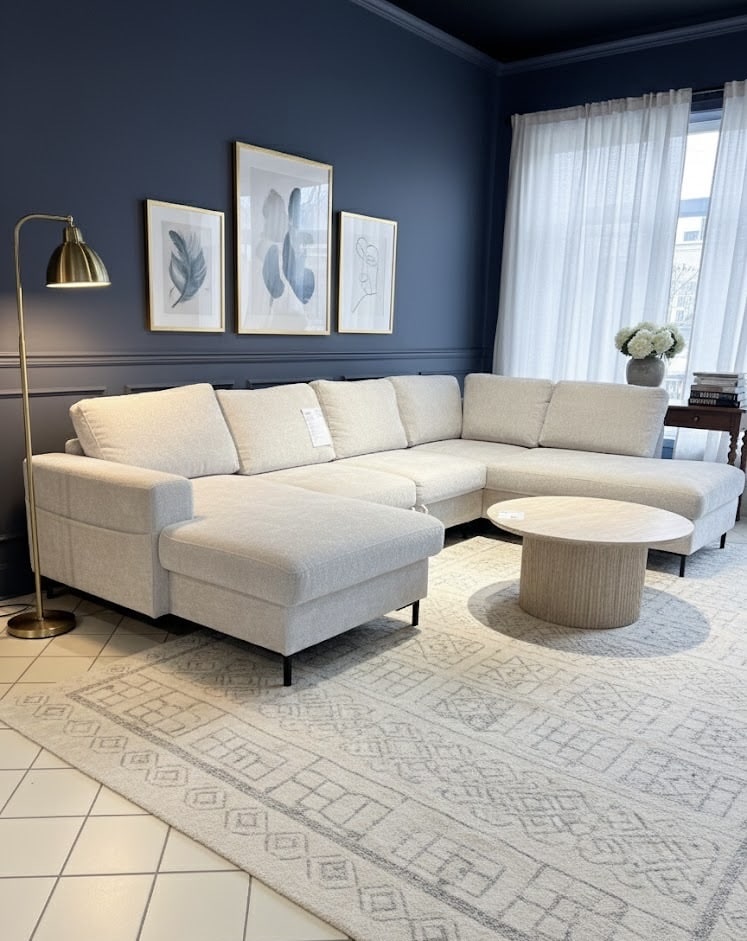 Canapé d'angle beige dans un salon bleu marine élégant avec tapis à motifs, table bois et lampe dorée.