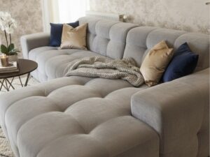 Canapé d'angle gris capitonné avec coussins bleus et dorés dans un salon élégant au papier peint floral.