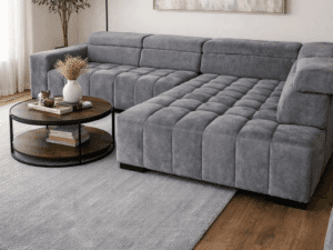 Canapé d'angle gris capitonné dans un salon moderne avec tapis, table basse en bois et grand tableau abstrait.