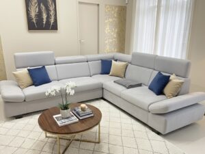 Canapé d'angle gris clair avec coussins bleus et beiges, table basse ronde en bois et orchidée blanche.