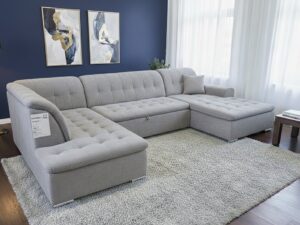 Canapé d'angle en U gris clair capitonné sur tapis épais, salon moderne au mur bleu marine et déco élégante.