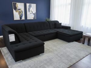 Canapé d'angle en U noir capitonné sur tapis gris dans un salon moderne aux murs bleu marine et cadres dorés.