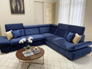 Canapé d'angle en velours bleu marine avec coussins dorés dans un salon élégant avec table basse ronde en bois.