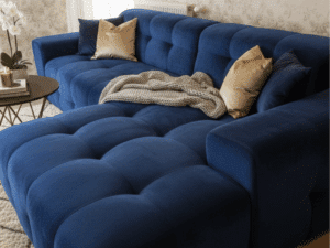 Canapé d'angle en velours bleu capitonné avec coussins dorés et plaid dans un salon à la déco élégante.