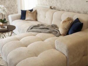 Canapé modulable crème capitonné dans un salon chic avec décoration murale dorée et coussins bleu marine et or.