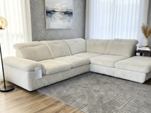 Canapé d'angle en velours côtelé beige dans un salon moderne avec tapis gris à motifs et mur texturé.