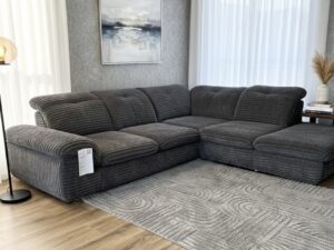 Canapé d'angle en velours côtelé gris anthracite sur un tapis texturé dans un salon moderne et lumineux.