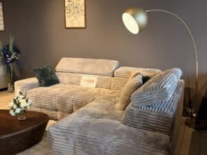 Canapé d'angle en velours côtelé gris avec coussins, table basse en bois et lampadaire design, affiché à 1 490€.