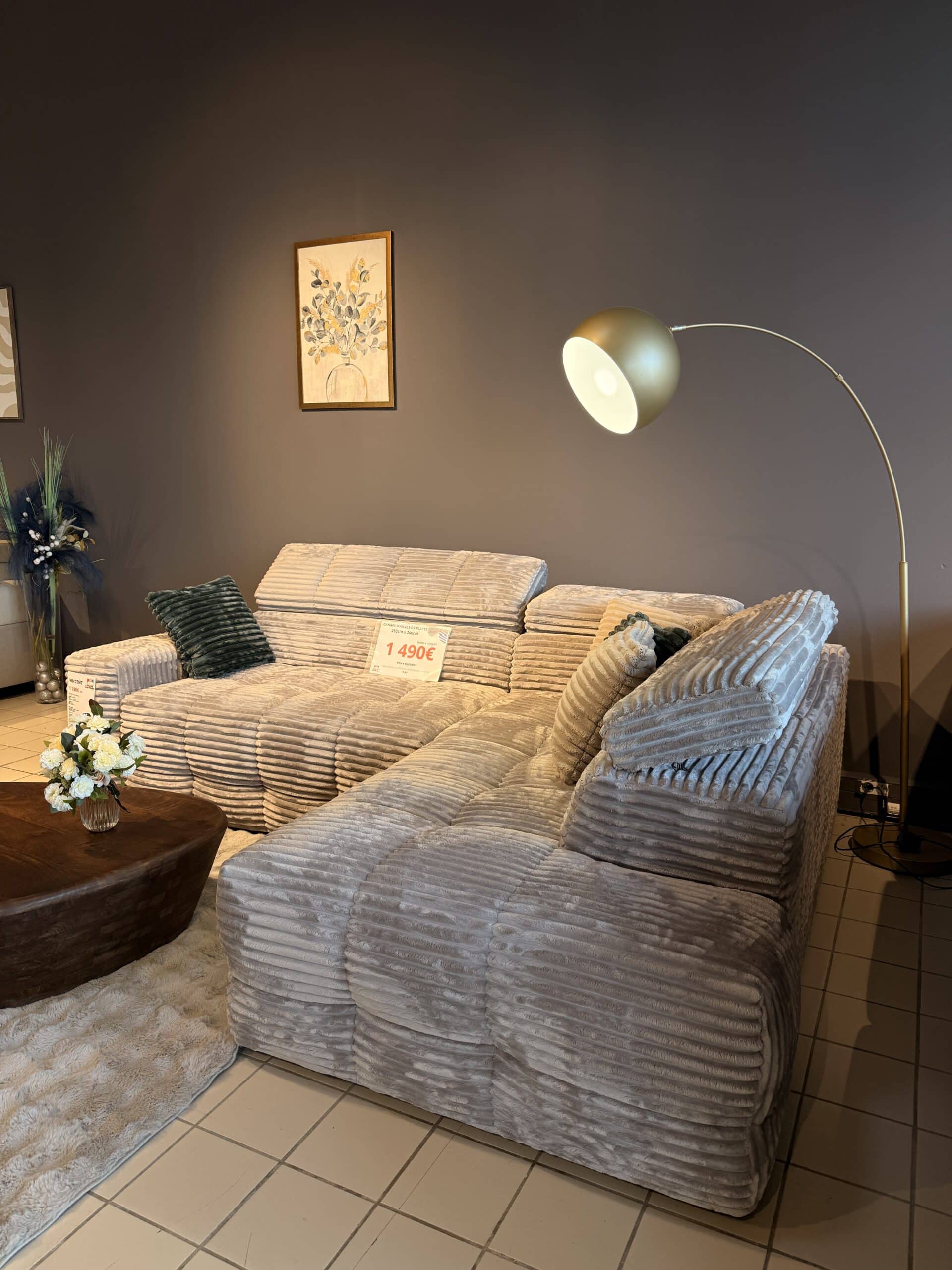 Canapé d'angle en velours côtelé gris avec coussins, table basse en bois et lampadaire design, affiché à 1 490€.