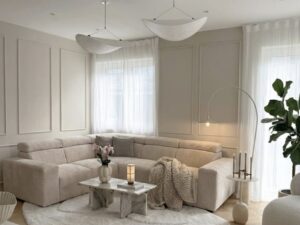 Salon minimaliste beige avec canapé d'angle côtelé, table en marbre, luminaires design et parquet en chevrons.