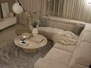 Salon moderne au style épuré avec canapé d'angle beige, table en travertin et tapis gris chaleureux.