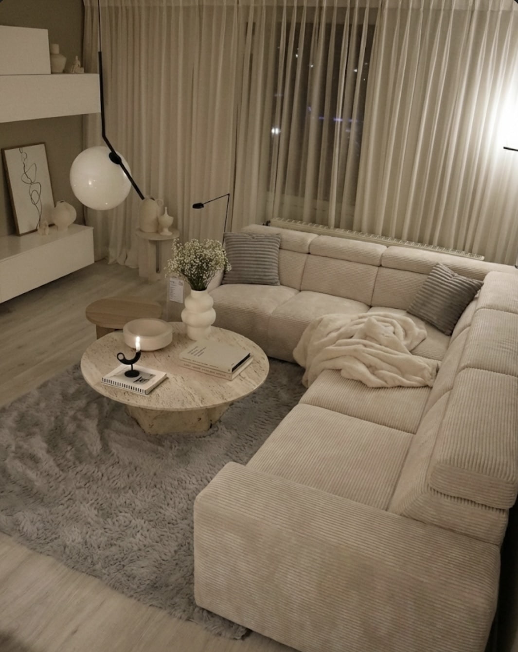 Salon moderne au style épuré avec canapé d'angle beige, table en travertin et tapis gris chaleureux.